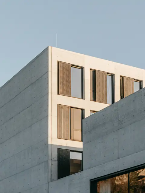Raw concrete building with timber shutters against a clear sky