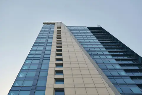 Glass and stone office tower rising against a pale blue sky