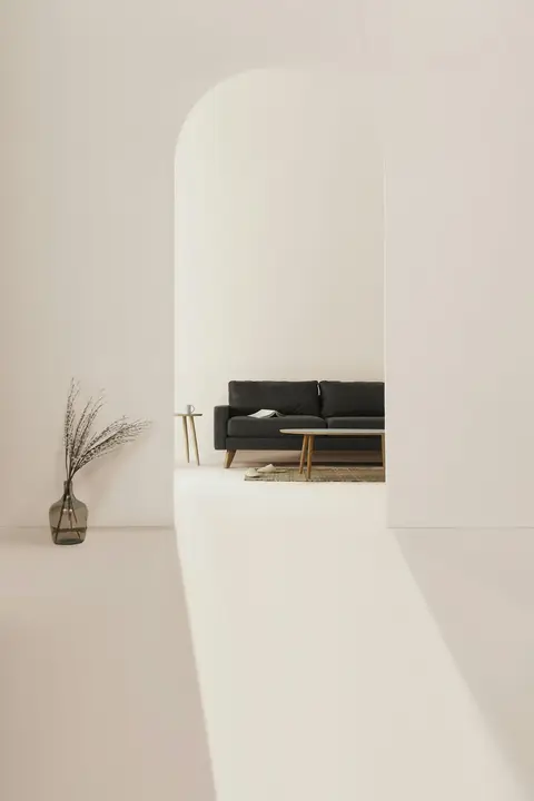 Soft plaster archway framing a black leather sofa in a sunlit room